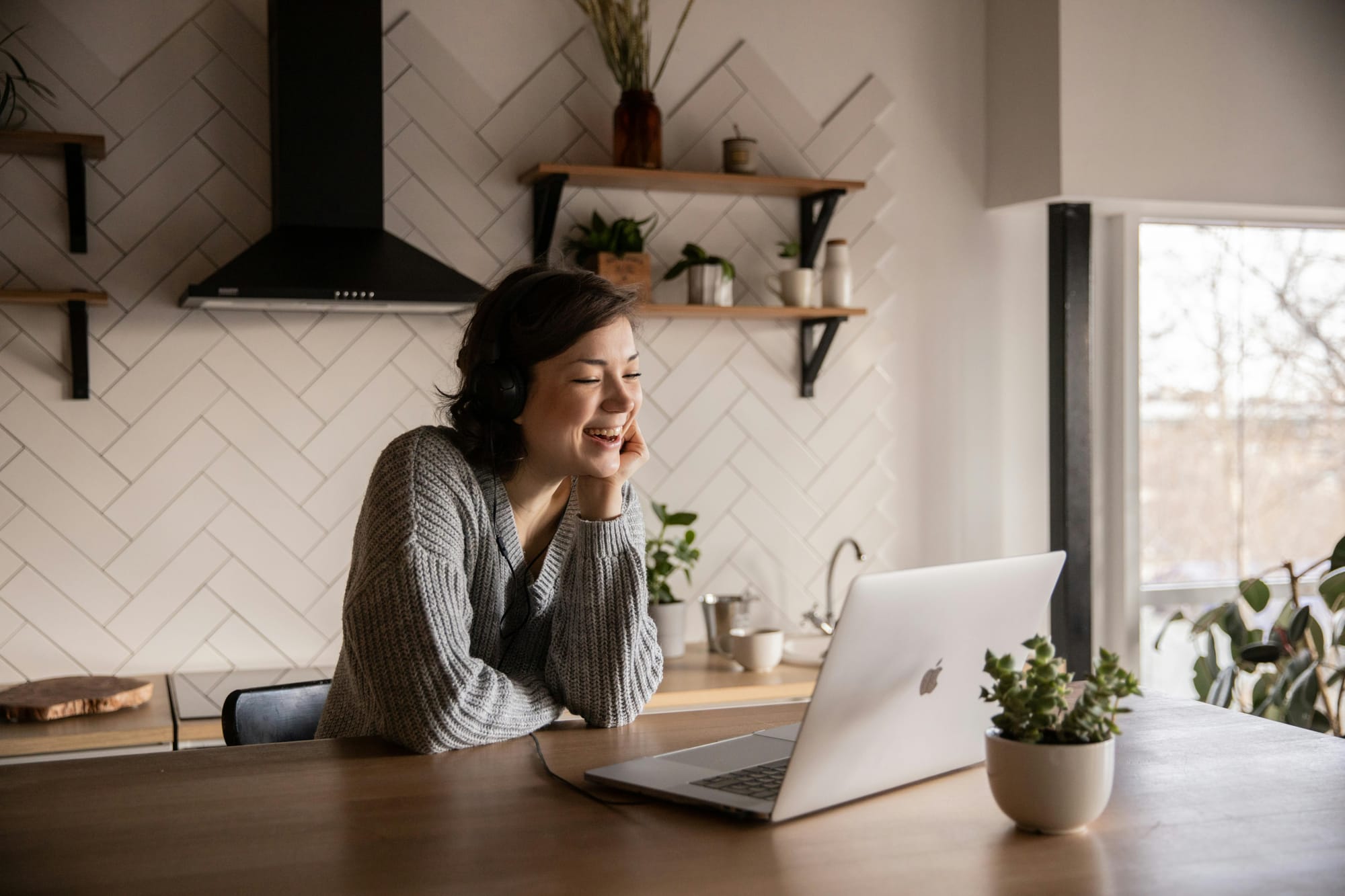 Woman sitting in a kitchen and smiling at a laptop screen