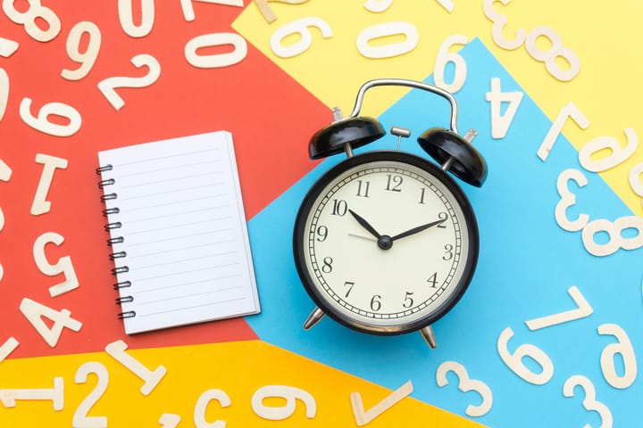 Image of blank notebook and an alarm clock with scattered numbers in the background